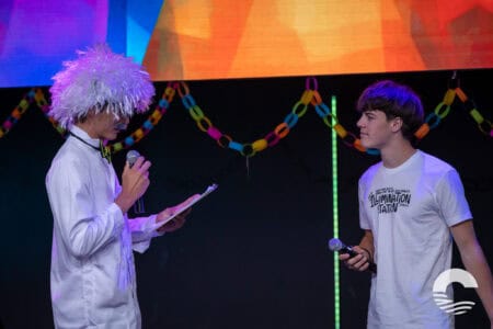 Two young men on stage at Canyon Springs Church youth event, one reading, the other holding a microp.