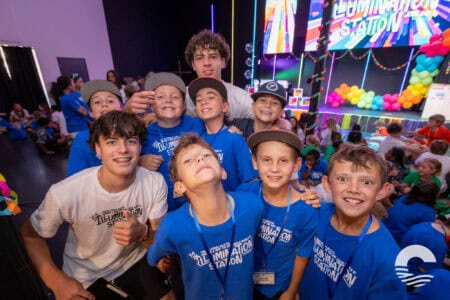 Group of smiling children at Canyon Springs Church youth event with stage and colorful decorations.