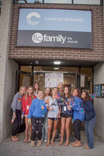 Group of diverse youth smiling and blowing bubbles outside Canyon Springs Church entrance.